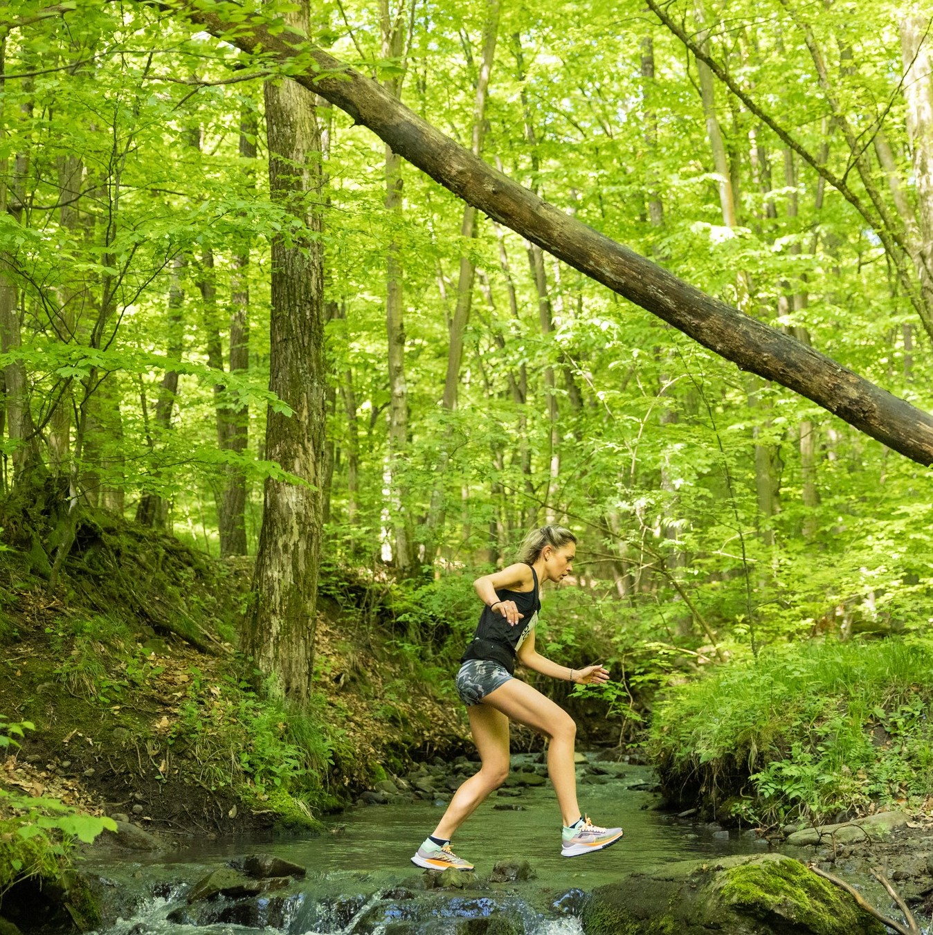 Julienn jumping across a forest stream during a trail run in the Hungarian hills